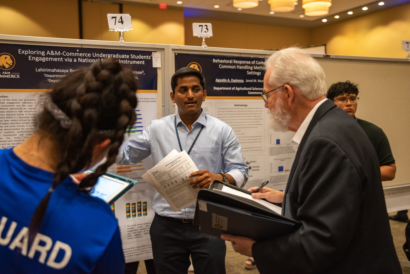 Student stands in front of his poster presentation as he answers a question from a judge. 