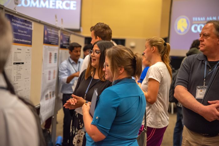 Several students and symposium attendees view research project posters.