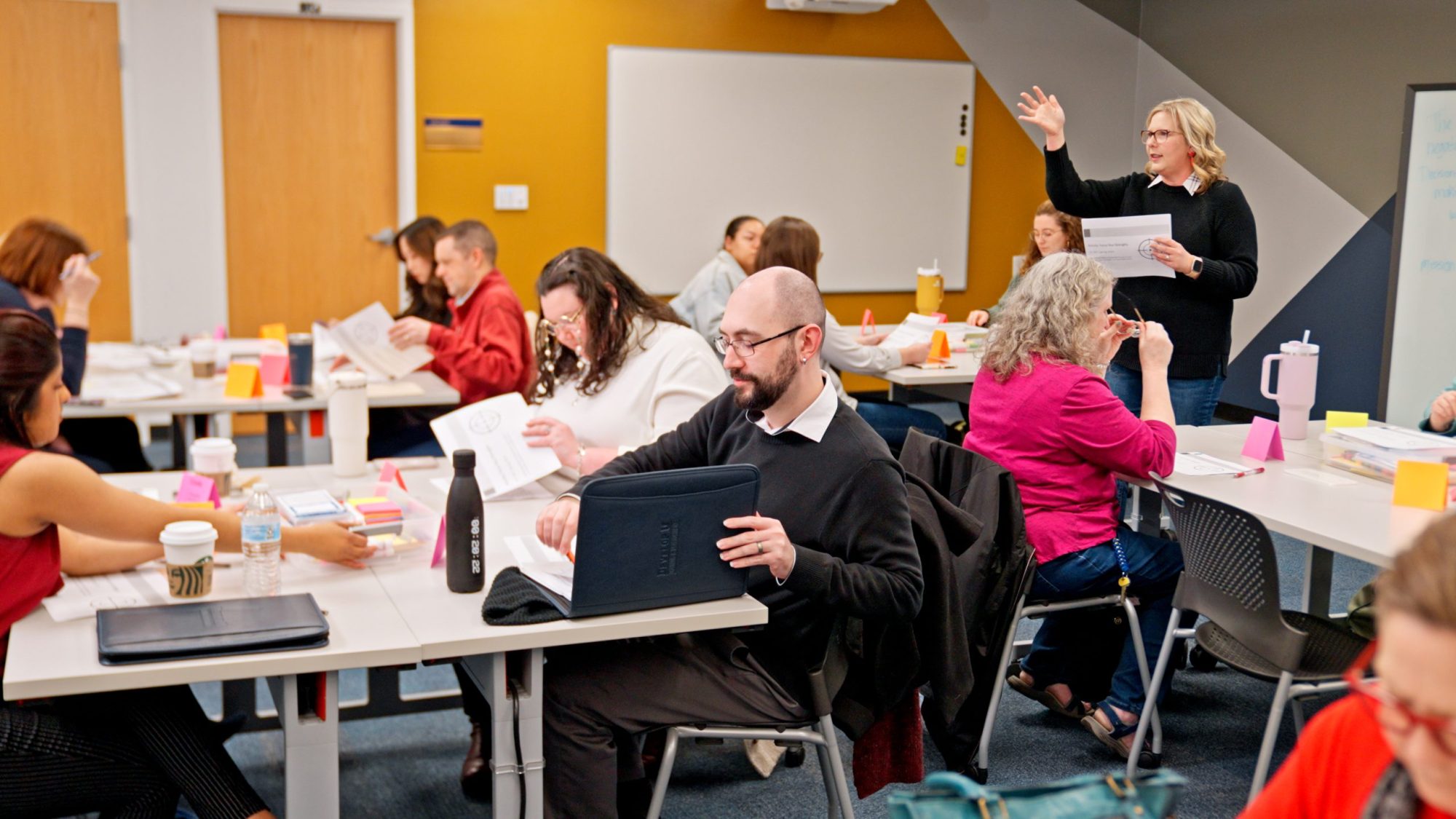 An instructor stands at the front of a packed room of adult students who are participating in a learning activity.