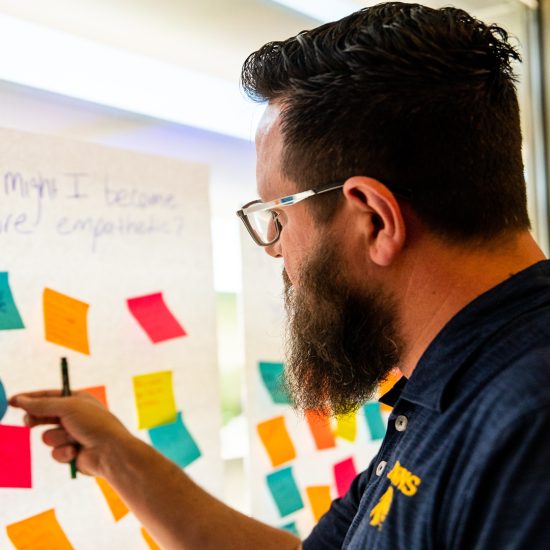 A man attaches sticky notes to a large white paper adhered to a large window.