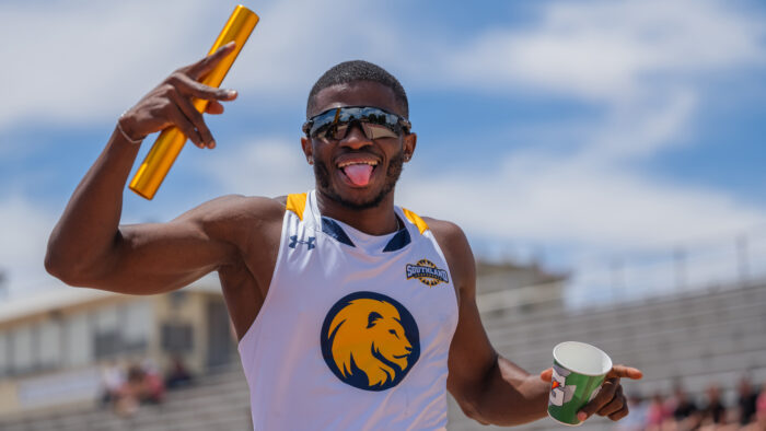 A track and field athlete holding a running baton celebrating.