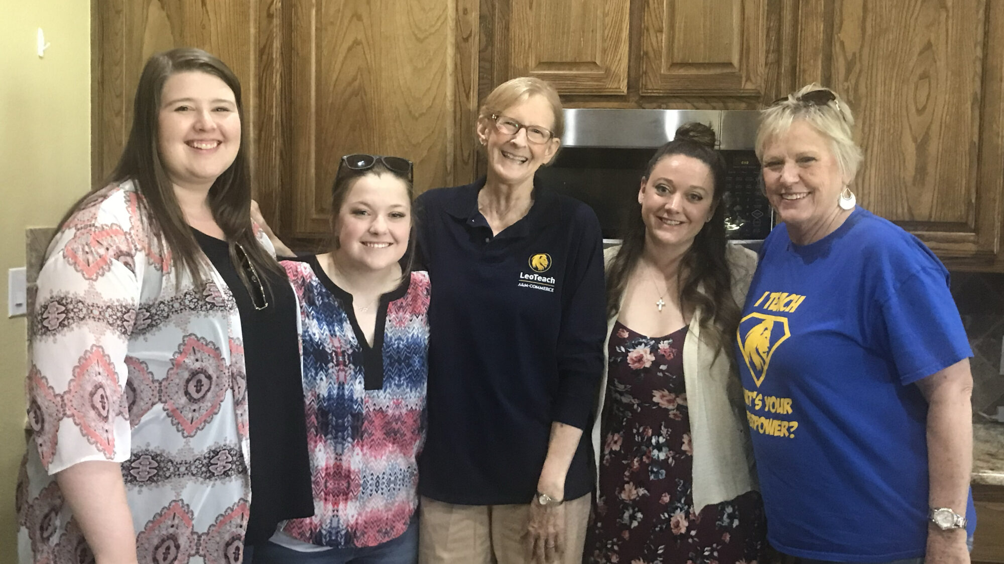 Five women stand smiling, shoulder-to-shoulder for a group photo.