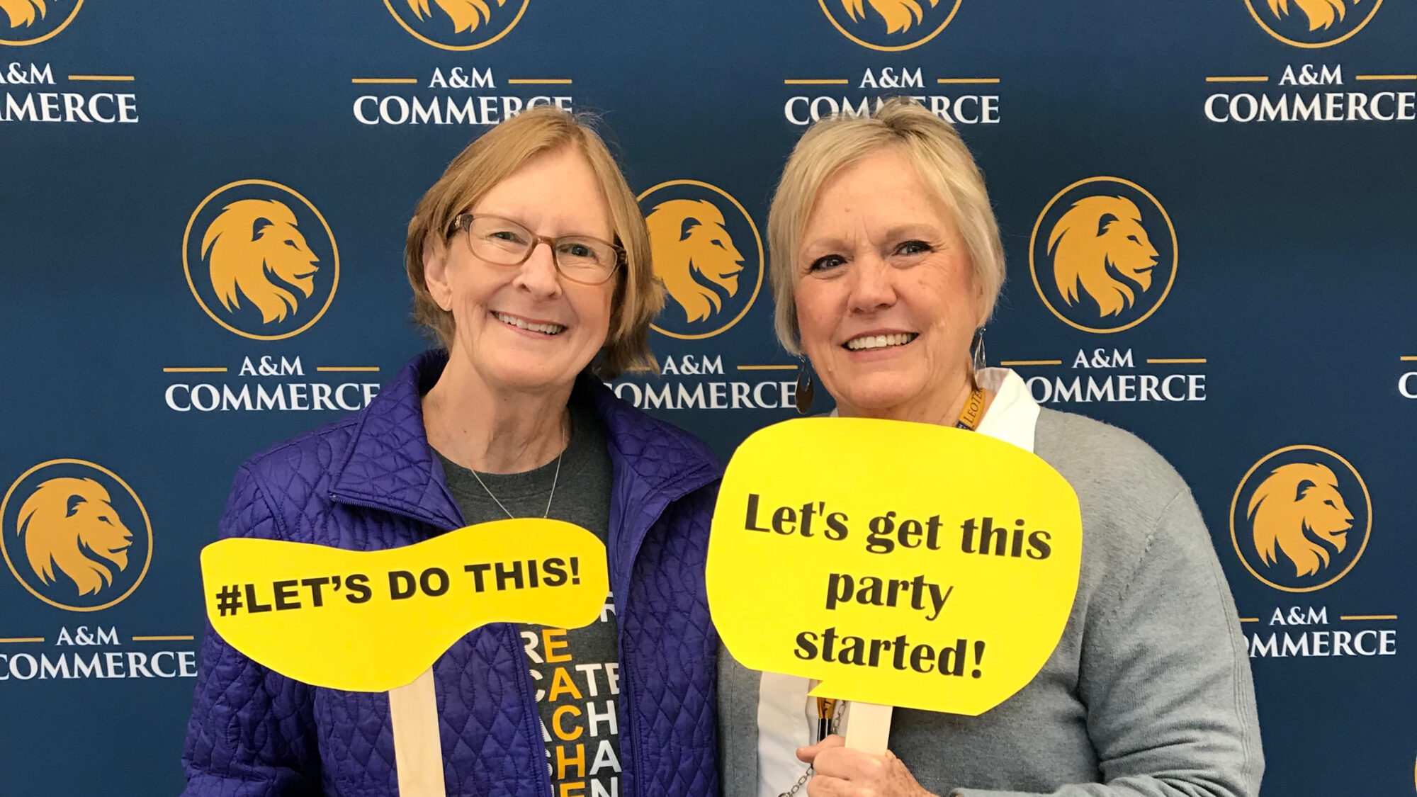 From left, former ETAMU faculty Drs. Kit Blount and Donna Tavener hold handcut yellow signs with words #LET'S DO THIS! and "Let's get this party started!".