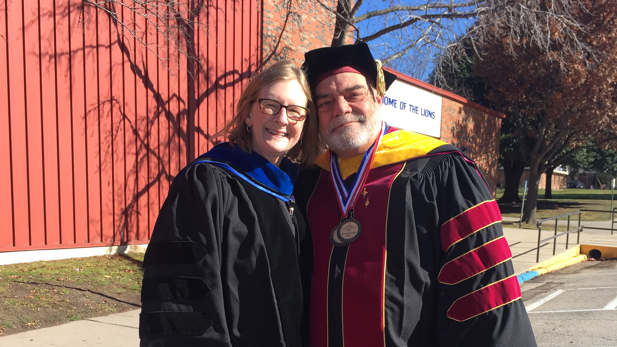 Two faculty stand side-by-side in graduation regalia.