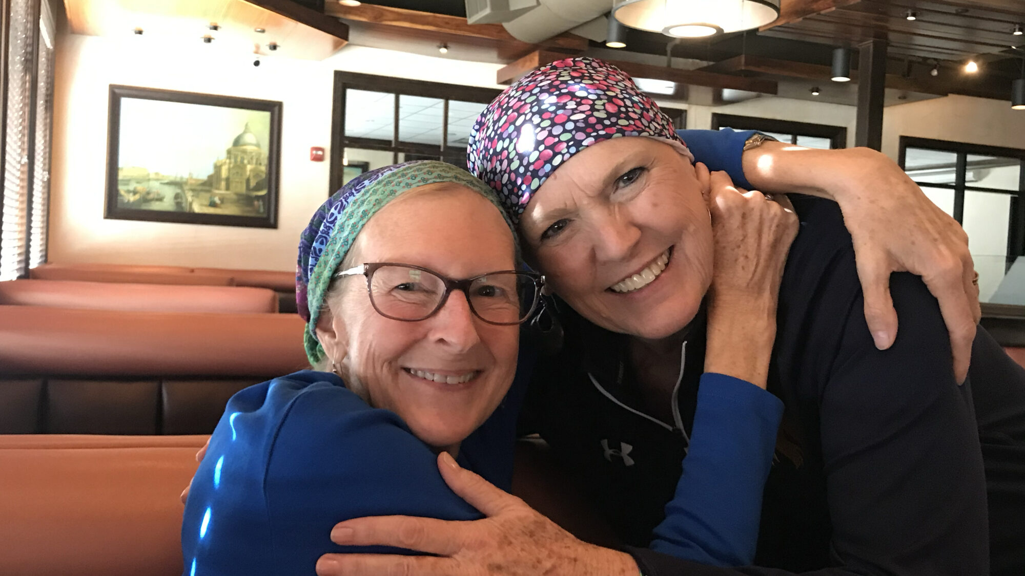 Two women wearing medical scrub hats embrace each other while smiling at the viewer.