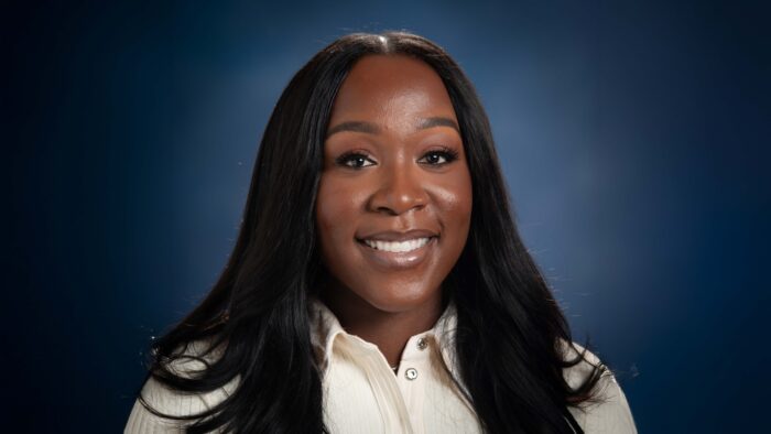 Headshot photo of woman smiling, wearing a white shirt and with a blue background.